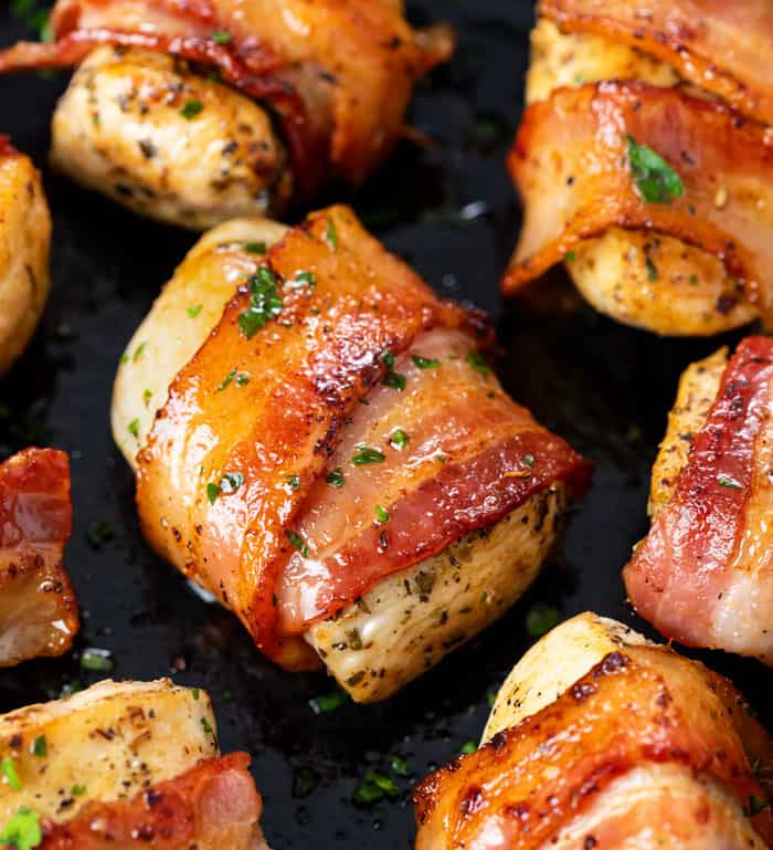 Seasoned chicken wrapped with crispy bacon in a skillet with parsley.