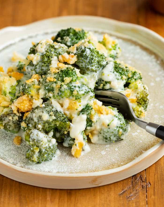 A plate with cheesy baked broccoli topped with ritz crackers with a fork on the side.