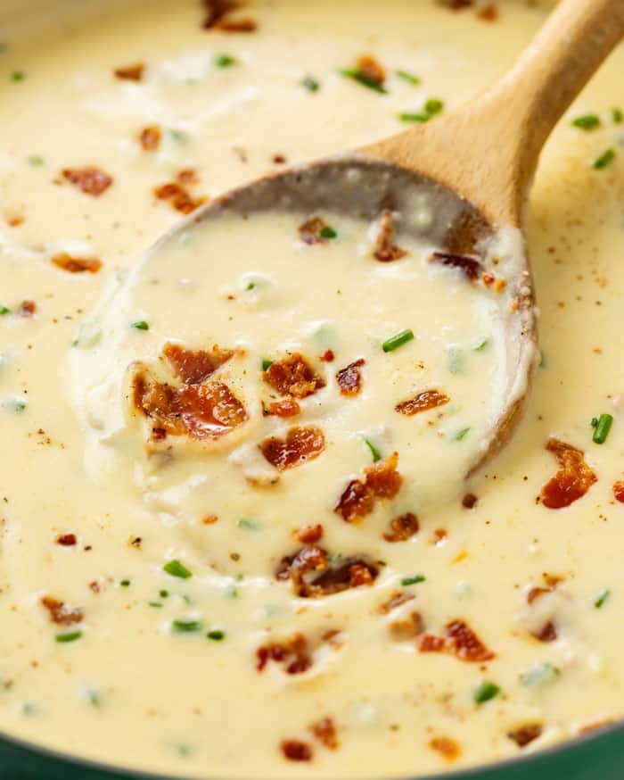 A wooden spoon scooping up baked potato soup topped with bacon and chives.