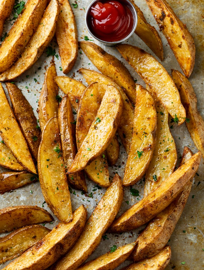 Crispy Baked Potato Wedges on a baking sheet with a ramekin of kethcup.