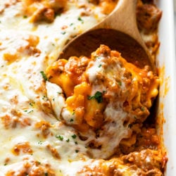 A wooden spoon scooping up baked ravioli from a casserole dish.