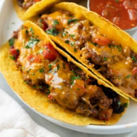 Baked Tacos with ground beef and melted a cheese on a white plate with cilantro on top.