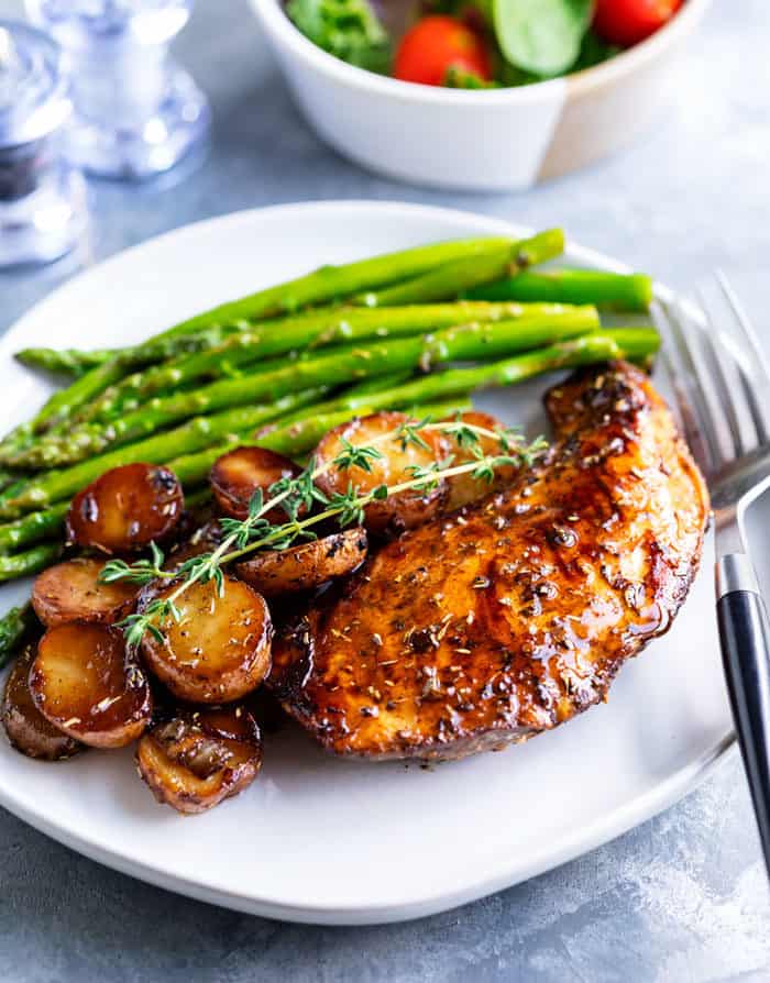 Balsamic chicken on a white plate with potatoes and asparagus.