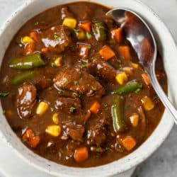 A bowl filled with Beef Vegetable Soup with a spoon in it.