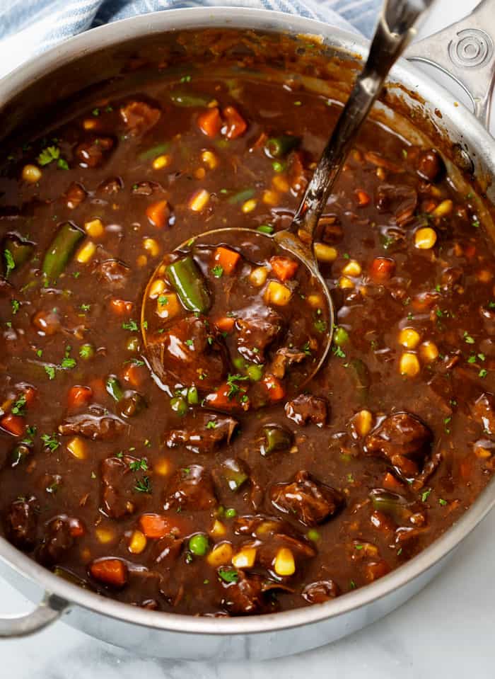 A pot filled with Beef Vegetable Soup with a ladle in it.