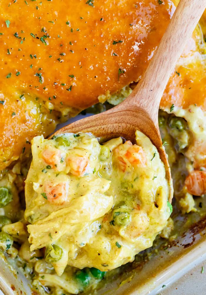 Wooden spoon scooping out chicken pot pie filling from a casserole dish.