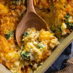 A wooden spoon with a scoop of broccoli chicken rice casserole from a casserole dish.