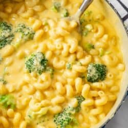 A spoon in a dutch oven filled with broccoli mac and cheese.