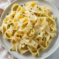 A white plate with buttered noodles topped with herbs.