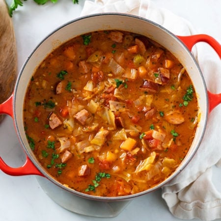 A red Dutch oven filled with Cabbage Soup with vegetables and Kielbasa.