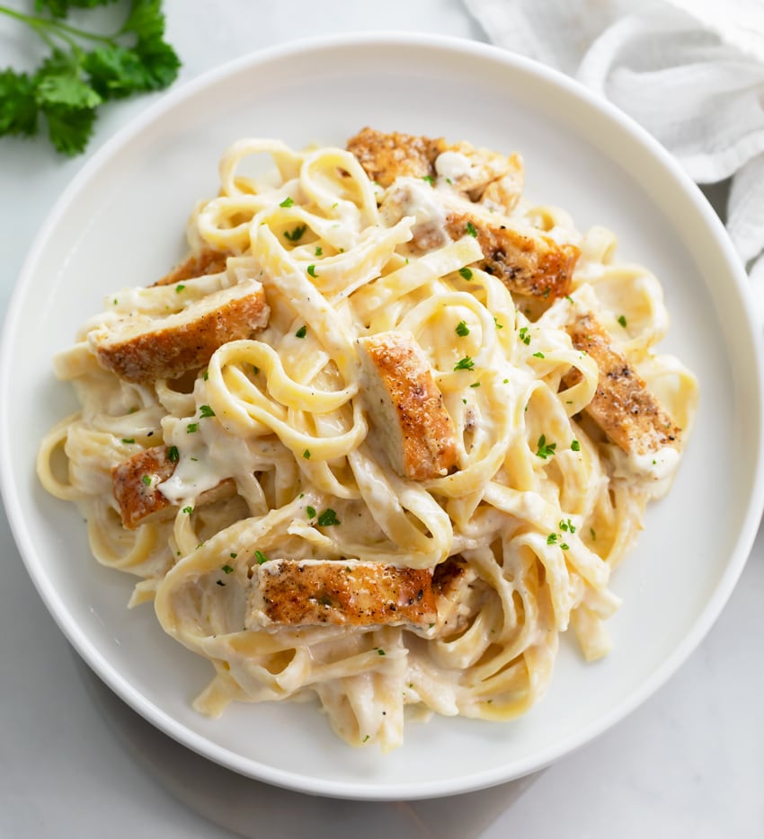 Chicken Alfredo Pasta on a white plate with parsley on top.