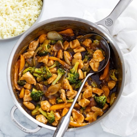 A skillet filled with Chicken and Broccoli with a spoon in it.