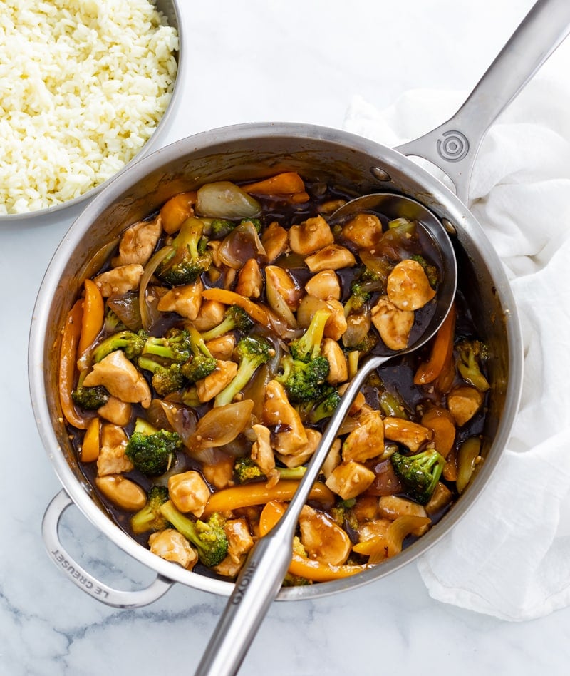 A skillet filled with Chicken and Broccoli with a spoon in it.