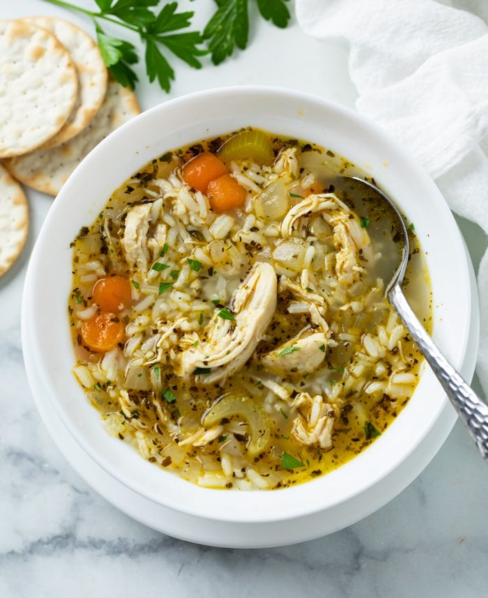 A white bowl filled with chicken and rice soup with a spoon on the side.