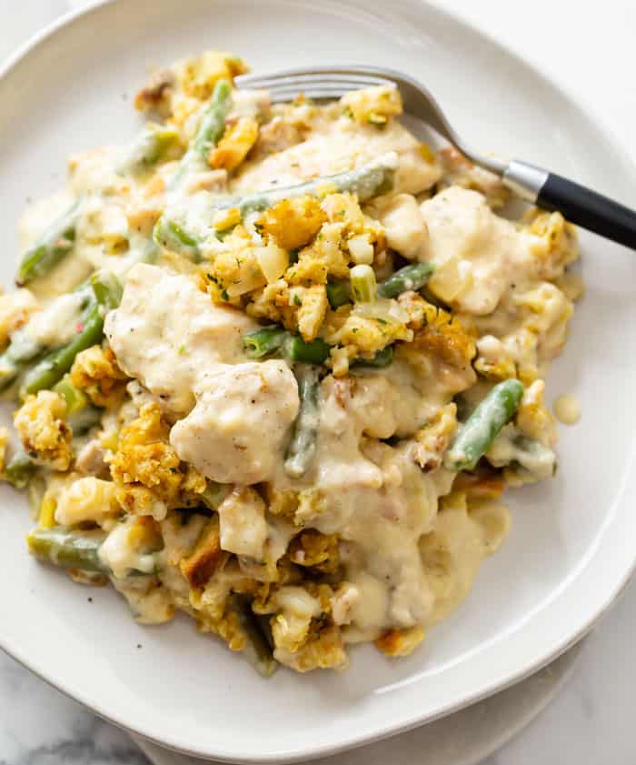 A white plate with Chicken and Stuffing Casserole and green beans with a fork.