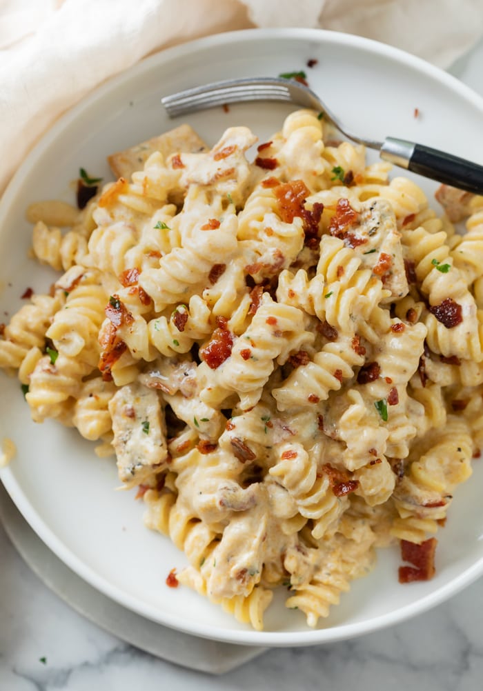 A white plate topped with creamy Chicken Bacon Ranch Pasta with crispy bacon on top.