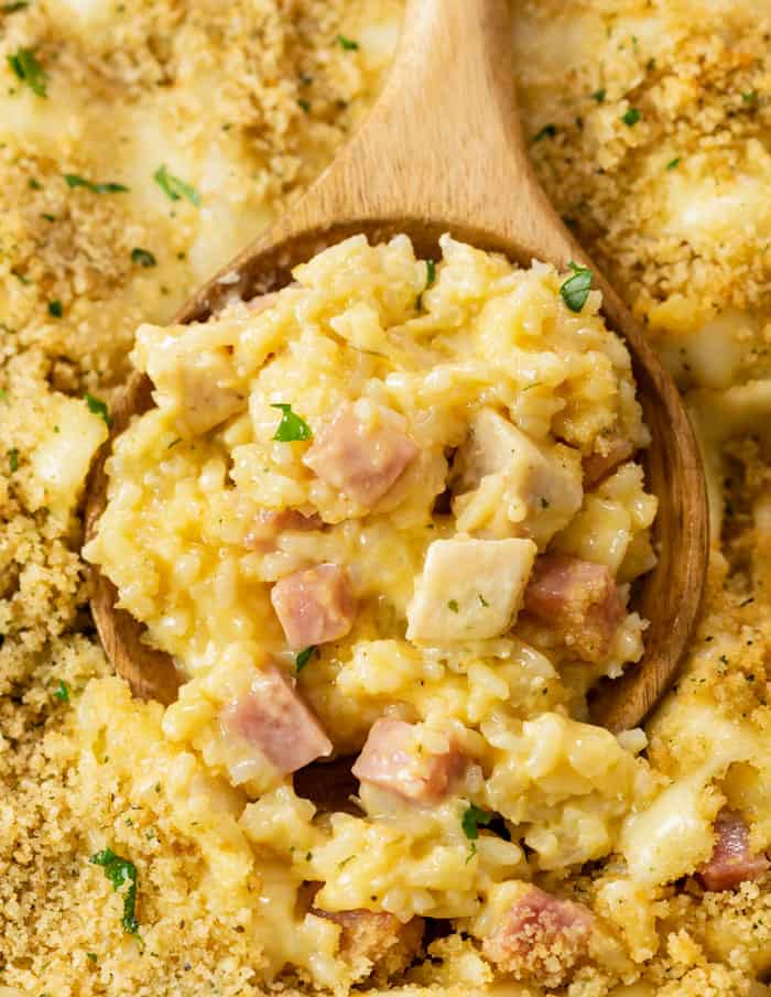 A wooden spoon scooping Chicken Cordon Bleu Casserole from a casserole dish.