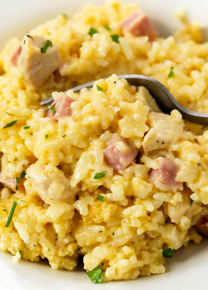 A white plate with a fork scooping up Chicken Cordon Bleu Casserole with ham, chicken, and rice.