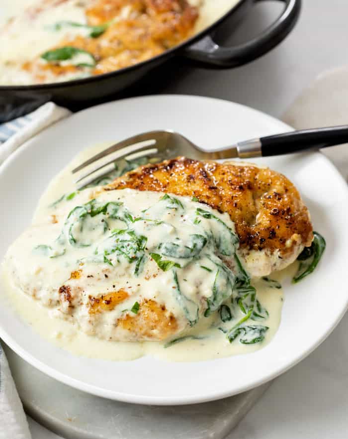 Chicken Florentine on a white plate with sauce on top and a fork in the back.