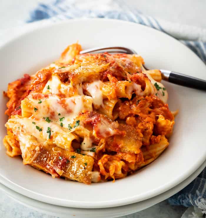 A white plate filled with rigatoni pasta with marinara sauce chicken Parmesan, and melted cheese.