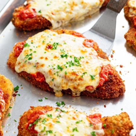 Chicken Parmesan on a tray with marinara sauce, mozzarella, and fresh parsley.