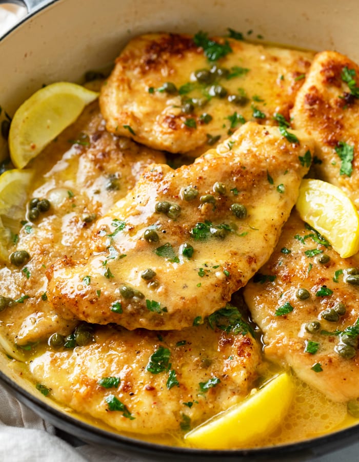 A pot with crispy Chicken Piccata in a white wine butter sauce with lemon wedges and capers.