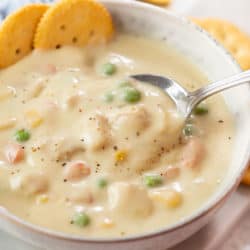 A spoon scooping up Chicken Pot Pie Soup from a bowl with crackers in the background.