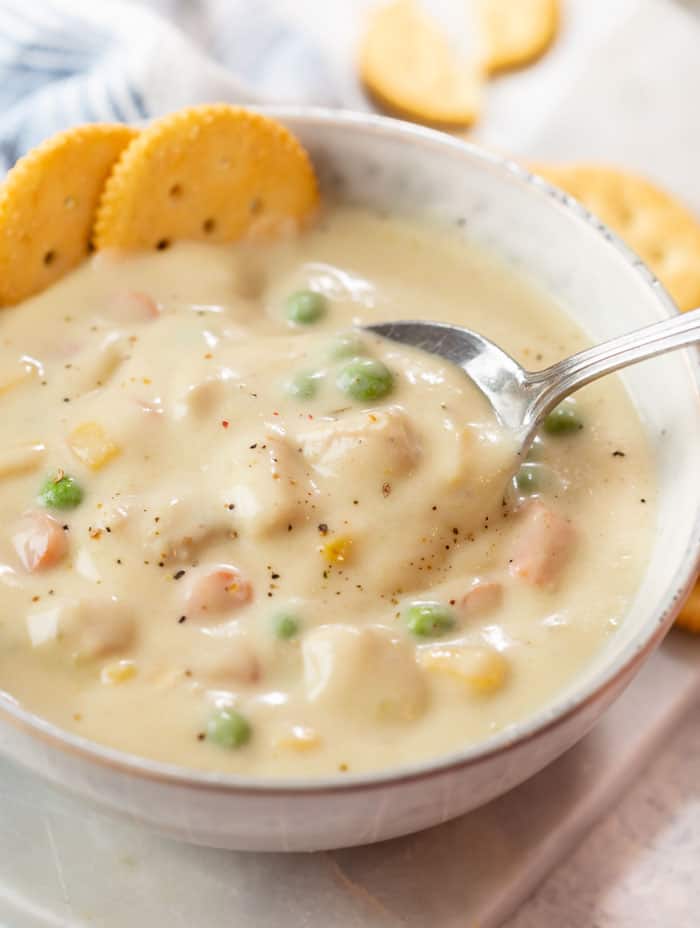 A spoon scooping up Chicken Pot Pie Soup from a bowl with crackers in the background.