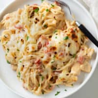 A white plate with cheesy Chicken Spaghetti with a fork on the side.