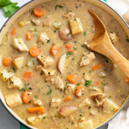 A Dutch oven filled with Chicken Stew with a wooden spoon in it.