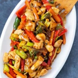 Overhead view of a white platter with chicken stir fry covered in sauce.