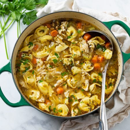 A soup pot filled with Chicken Tortellini Soup with a ladle in it.