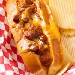 A Chili Cheese Dog in a red serving basket with potato chips.