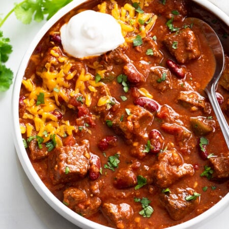 A white bowl filled with Chili Con Carne with cheese and sour cream.