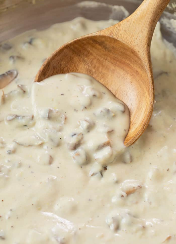 A wooden spoon scooping condensed cream of mushroom soup up from a pan.