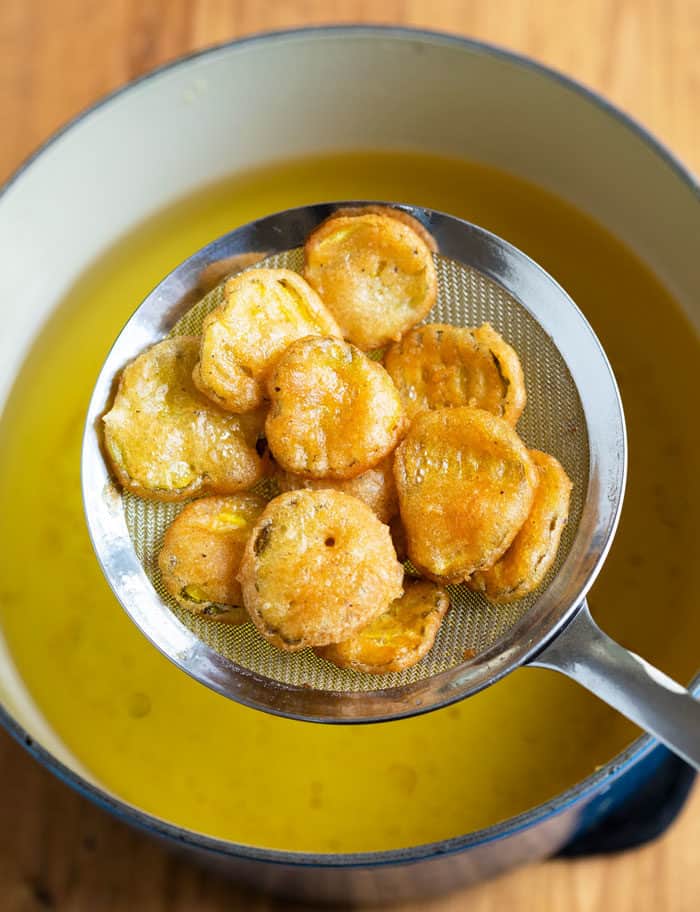 A spider strainer filled with fried pickles being pulled up from oil after bring fried.