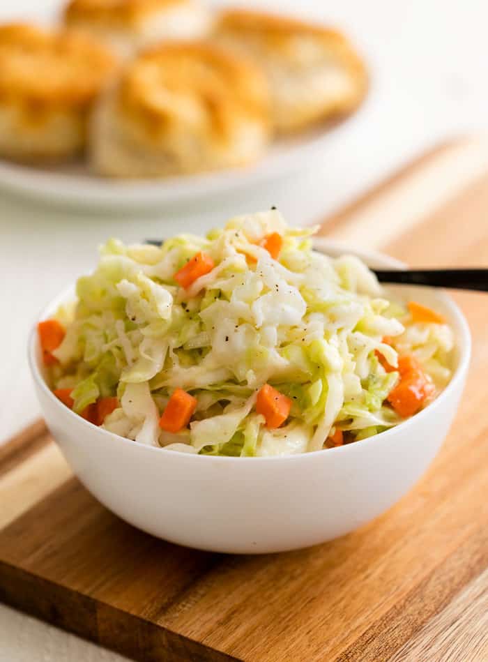 White bowl filled with Copycat KFC Coleslaw on a wooden cutting board with biscuits in the background.