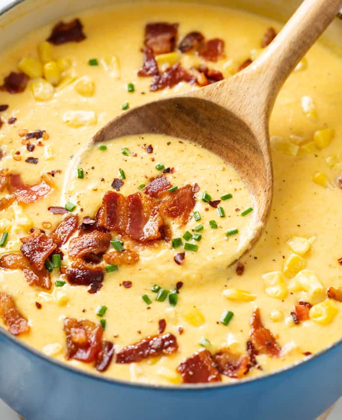 A soup pot filled with homemade Corn Chowder topped with bacon, chives, corn, and red pepper flakes.