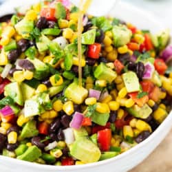 A white bowl filled with cowboy caviar with dressing being drizzled on top.