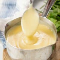 A spoon pulling up thick and smooth cream of chicken soup from a saucepan.