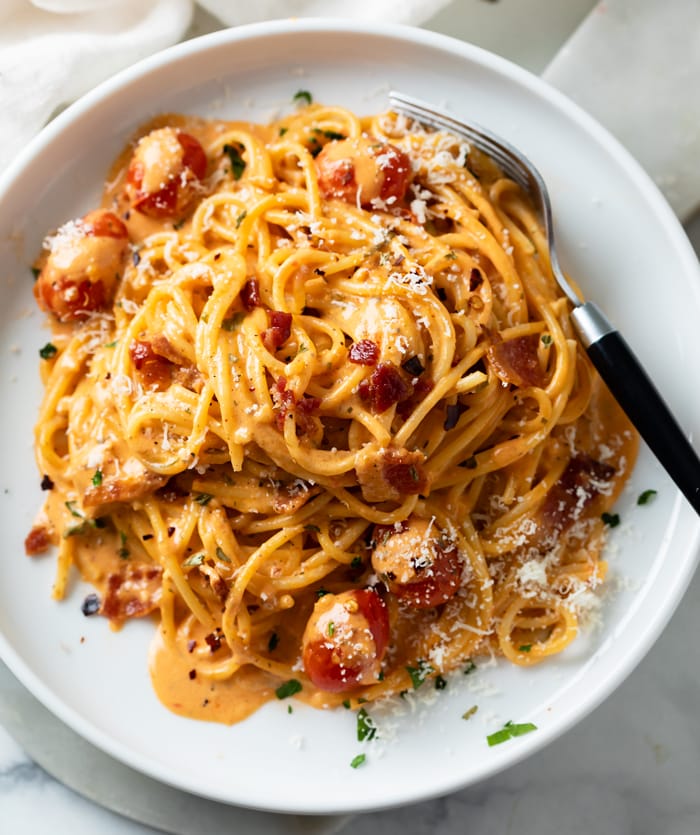 A white plate with creamy bacon pasta on it with spaghetti and crispy bacon.