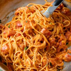 A skillet with creamy tomato pasta with kitchen tongs.