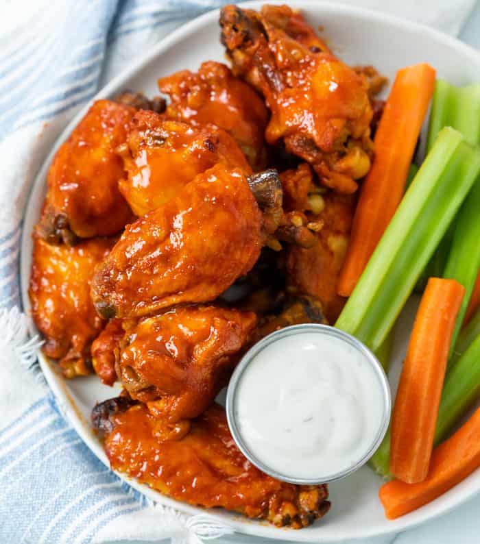 A plate with Buffalo Chicken Wings with a cup of blue cheese with celery and carrot sticks.