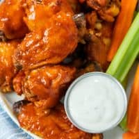 A plate with Crock Pot Chicken Wings next to a cup of blue cheese with celery and carrot sticks.