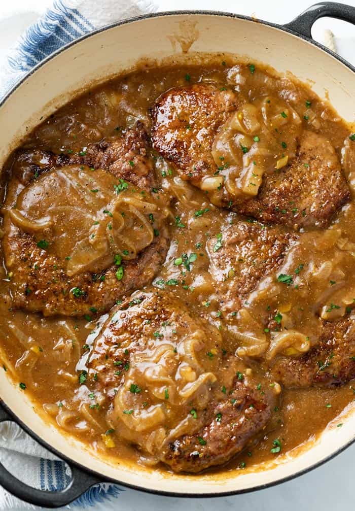 A skillet with cube steak smothered in brown gravy with parsley on top.