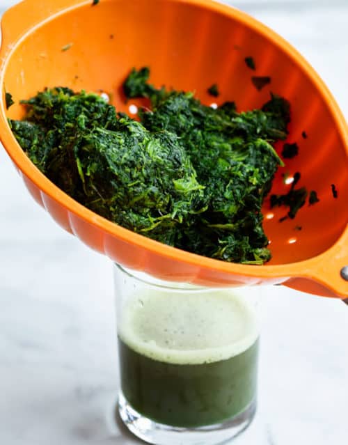 Spinach in an orange strainer over a cup to have water removed.