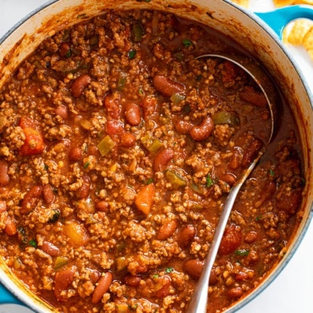 A pot filled with Chili with a ladle in it and Fritos on the side.