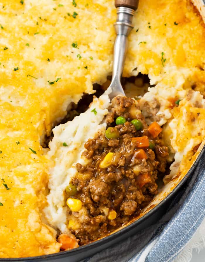 A large spoon scooping Shepherds Pie from a casserole dish.