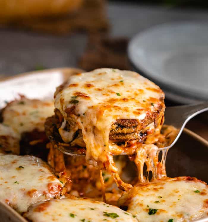 A spatula holding up warm, cheesy eggplant Parmesan. 