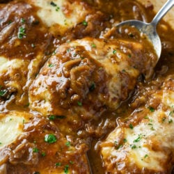 A spoon scooping up French Onion Chicken from a skillet with melted cheese on top.